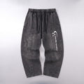 Dark gray washed denim pants with an elastic waistband and a white vertical graphic logo on the left leg, laid flat against a light gray background.