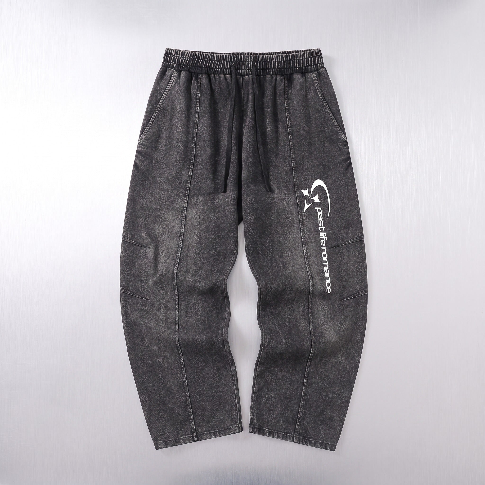 Dark gray washed denim pants with an elastic waistband and a white vertical graphic logo on the left leg, laid flat against a light gray background.