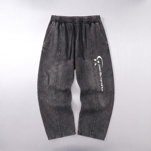 Dark gray washed denim pants with an elastic waistband and a white vertical graphic logo on the left leg, laid flat against a light gray background.